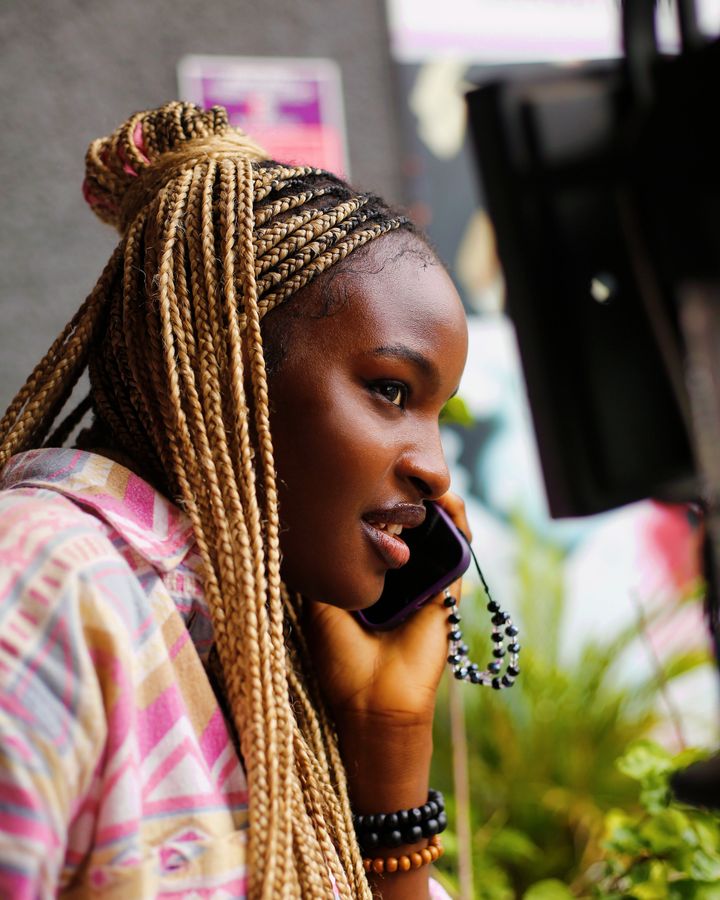 A young woman smiling while talking on her phone outdoors in Abuja