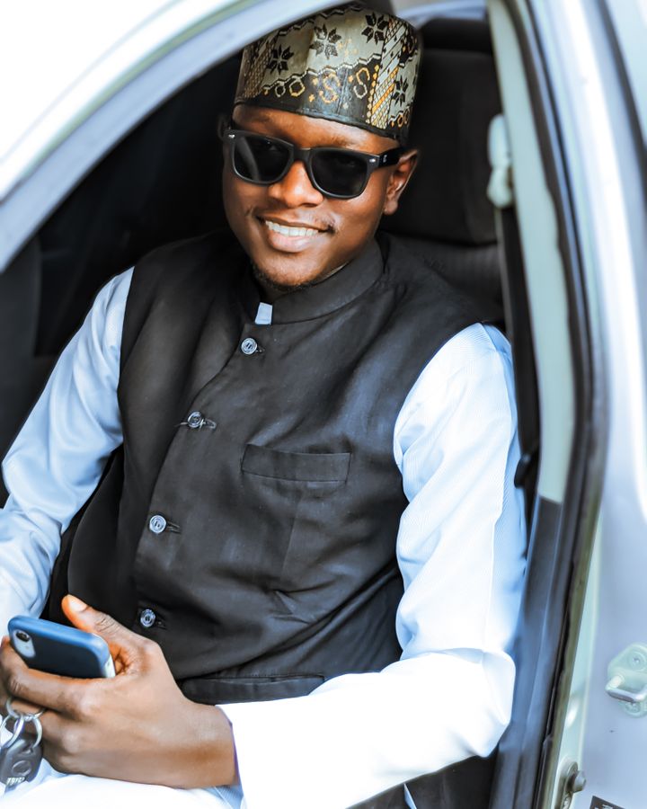 A man sitting in his car holding a phone and smiling